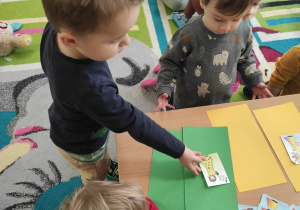 Zdjęcie Bartosza odkładającego zieloną karteczkę z obrazkiem Pani Wiosny na zieloną kartkę A4.