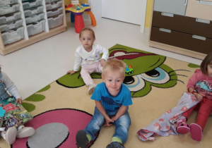 Zdjęcie dzieci z grupy Biedroneczki siedzących na dywanie podczas zajęć muzycznych.