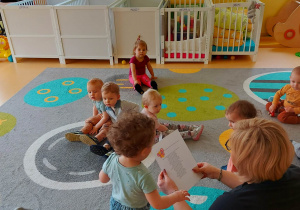 Opiekunka z grupy Motylki czyta dzieciom na dywanie wierszyk ,,Jak powstaje motyl?''.