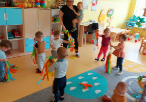 Zdjęcie dzieci i opiekunki podczas tańca z bibułowymi kolorowymi pomponami.