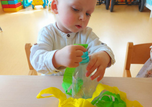 Maksymilian starannie wkłada zieloną bibułę do butelki.