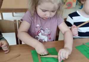 Zuzanna dokładnie przykleja łodyżkę bazi na swoją zieloną kartkę papieru.