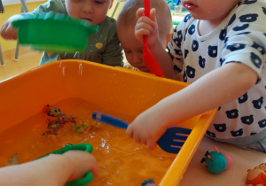 Szymon, Leon i Miłosz pozują do zdjęcia podczas zajęć z miską z wodą i pływającymi w niej zabawkami.