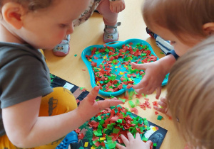 Dzieci podczas posypywania stworzonych koron drzew kolorowymi bibułami.