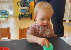 Zdjęcie Aleksandry podczas robienia stempelków za pomocą zielonej gąbeczki namoczonej w zielonej farbie.
