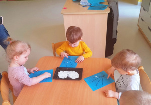 Dzieci siedzące przy stoliku podczas pracy plastycznej.
