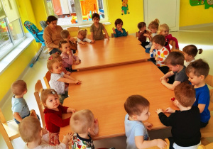 Dzieci z grupy Biedroneczki siedzące przy wspólnym stole tuż przed rozpoczęciem zajęć kulinarnych.
