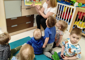 Opiekunka opisuje dzieciom przy pomocy książki zjawisko atmosferyczne, którym jest błyskawica.