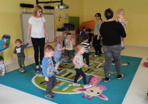 Dzieci razem z opiekunkami tańczą na dywanie do piosenki ,,Małe wygibasy''.