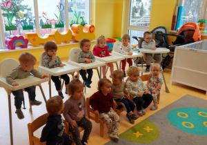 Zdjęcie dzieci siedzących w foteliczkach podczas teatrzyku prowadzonego przez opiekunki pt. ,,Narodziny Motyla''.