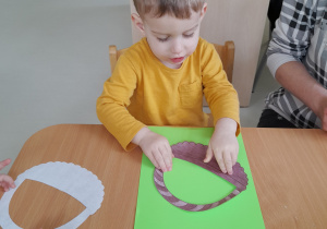 Aleksander przykleja papierowy koszyczek na zielony karton.