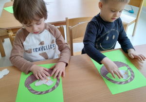 Maksymilian i Maciej wklejają papierowe baranki do szablonu koszyka.