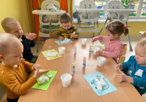 Dzieci z grupy Żabki siedzą przy stole podczas pracy plastycznej.