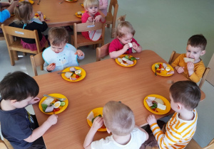 Dzieci siedzące przy wspólnym stole jedzą śniadanie wielkanocne.