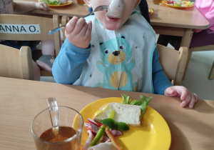 Zdjęcie Huberta jedzącego białą kiełbaskę nabitą na widelec.