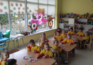 Zdjęcie dzieci z grupy Pszczółki siedzących przy stoliczku przed rozpoczęciem malowania jajek kolorowymi farbami.