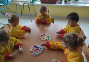Dzieci przy stoliczku starannie malują swoje jajeczka kolorowymi farbkami.