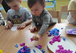 Zdjęcie Stanisława biorącego z papierowego talerzyka kawałeczki bibuły w kolorze fioletowym.