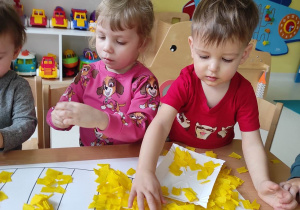 Alicja i Tymoteusz dekorują paski Pszczółki Mai żółtą bibułą.