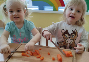 Uśmiechnięta Hanna i Maria pozują do zdjęcia podczas krojenia marchewki.