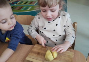 Alicja przytrzymuje ziemniaka rączką podczas próby przekrojenia go nożykiem.
