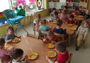 Zdjęcie dzieci siedzących przy stoliczku podczas jedzenia zrobionej przez nich sałatki.