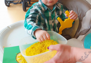 Opiekunka daje Wiktorowi żółty ryż w plastikowym pojemniku.