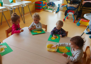 Zdjęcie dzieci siedzących przy stoliczku podczas wykonywania pracy pt. ,,Żółte Kurczątko''.