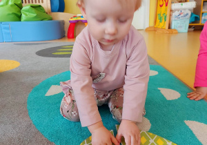 Aleksandra układa na dywanie puzzle w kształcie zielonej pisanki.
