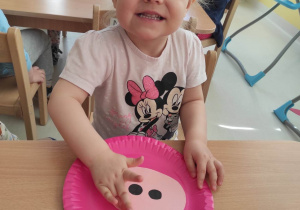 Hanna pozuje do zdjęcia podczas przyklejania ryjka na różowy talerzyk.