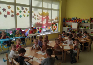 Zdjęcie dzieci siedzących przy stoliczku przed rozpoczęciem wykonywania pracy plastycznej pt. ,,Wiejska Krówka''.