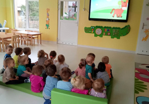 Zdjęcie dzieci siedzących na materacu podczas oglądania filmiku edukacyjnego.