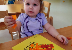 Lila pozuje do zdjęcia z pomarańczową bibułą w rączce.