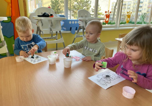 Troje dzieci siedzących przy stoliku podczas pracy plastycznej.