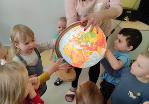 Zdjęcie dzieci próbujących kręcić trzymanym przez opiekunkę globusem.