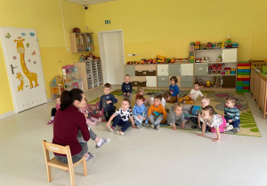 Opiekunka opowiada dzieciom siedzącym na dywanie o przyrodzie.