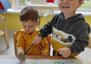 Artur maluje pędzelkiem zamoczonym w zielonej farbie dłoń Tymoteusza.