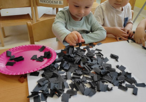 Mały Stanisław przykleja samodzielnie na szablon kubła kwadraciki z czarnej bibuły.
