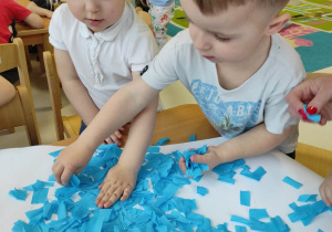 Fotografia Hanny i Bartosza podczas wspólnego przyklejania na narysowany szablon kubła niebieskiej bibuły.