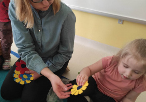 Opiekunka daje Zuzannie żółty kwiatuszek.