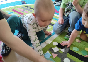 Bartosz z pomocą opiekunki kładzie malutki trójkącik na szablonie dużego trójkąta.