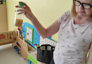 Jedna z opiekunek pokazuje dzieciom plastikową buteleczkę z płatkami kukurydzianymi.