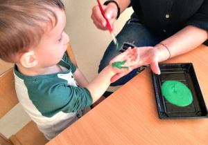 Opiekunka maluje pędzlem na zielono dłoń Aleksandra.