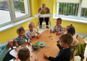 Zdjęcie dzieci siedzących przy stoliku podczas wyklejania papierowych rolek.