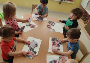 Zdjęcie dzieci siedzących przy stoliczku podczas układania puzzli z okazji Dnia Strażaka.