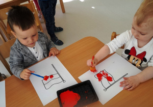 Fabian i Zoja za pomocą gąbki i czerwonej farby malują swoje flagi.