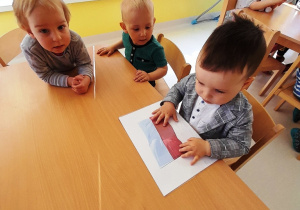 Troje dzieci przygląda się ilustracji z flagą Polski.