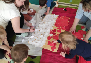 Opiekunki razem z dziećmi przyklejają na szablon flagi białe i czerwone serduszka.