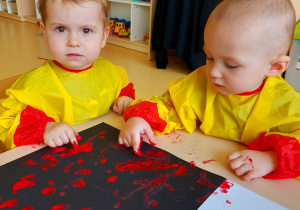 Szymon i Leon malują paluszkami z czerwoną farbą szablon flagi Polski.