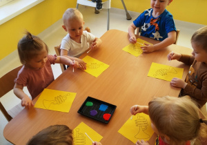 Dzieci z żółtymi kartkami siedzą przy stole podczas zajęć.